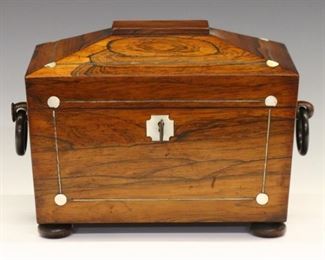 Lot 29: An early 19th century British William IV Period tea caddy.  Rosewood case in sarcophagus form with Silver stringing, inlaid Mother of Pearl medallions and escutcheon, turned ring handles and flattened ball feet.  Opens to reveal single tea box and cut glass mixing bowl.  Older finish with minor wear.  9 x 6 x 7" high overall.  ESTIMATE $400-600