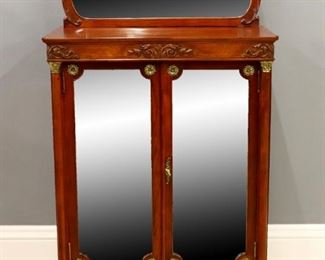 Lot 33: A turn of the century American Louis XVI style side cabinet. Mahogany construction features a shaped back with carved foliate detail and shaped beveled mirror.  Two door base with shaped beveled mirrors open to reveal an interior fitted with adjustable shelves and lower compartments, flanked by slender fluted columns with Brass capitols and bases on delicate turned feet with Brass caps.  Older refinishing with minor wear.  28 3/4 x 16 1/2 x 40 3/4" high overall.  ESTIMATE $600-800