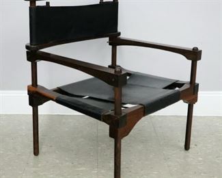 Lot 54: A 1960's Don Shoemaker for Senal S.A. (Mexico)  "Perno" Safari armchair.   Mexican Cocobolo wood construction with Black leather sling back and seat.  Wood frame with some marks and scuffs to finish, leather sling seats with scattered points of wear and some fading to the original leather dye, one seat stretcher strap replaced.  23 x 21 × 28 1/4" high overall.  ESTIMATE $1,500-2,500