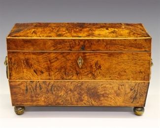 Lot 98: An early 19th century British tea caddy.  Burl wood case in sarcophagus form with molded top, Boxwood stringing, Brass lion's mask handles and ball feet.  Opens to reveal two tea boxes and compartment for a mixing bowl.  Polished finish with minor wear, slight veneer lifting.  12 x 6 x 7 1/2" high overall.  ESTIMATE $600-800