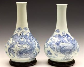 Lot 133: A pair of Korean Blue and White porcelain bottle vases.  Bulbous forms with slender necks, each decorated with a dragon chasing a flaming pearl through clouds.  Unmarked.  Minor wear overall, one with 1/2" hairline crack at rim, a few production glaze flaws and minor pitting, both with slight wear at rim and roughness at foot, no chips or repairs.  Up to 12 1/2" high plus stands.  ESTIMATE $600-800