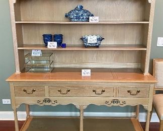Lot 9095. $275.00. Weiman Pickled Oak Side Board and Hutch.  Sideboard has three pull out drawers, scalloped trim below that and a base open shelf above the leg knobs and it appears to have a couple stencils .  Hutch has same Scalloped feature below the top of the unit, and two shelves and sits right on the sideboard.  I believe it might have a little water damage on the lower shelf. Sideboard measures 64"w x 20"d x 32.5" tall.  Hutch measures 63" w x 12"deep x 38"tall.  You can leave this precisely like this, or creative people may paint this in a fun way and change the hardware!  Great piece with good bones!