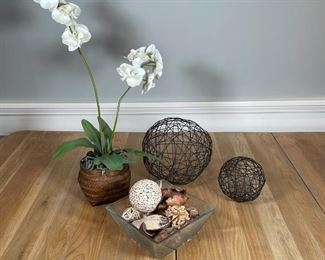 GROUP DECORATIVE ITEMS | Including a square glass bowl with wicker balls and organic décor (9 x 9 in.), a pair of black painted "woven" metal balls, and a faux orchid flower arrangement in a woven basket (h. 27 in.) 