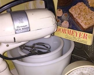 A 1940s Dormeyer mixer stands ready to mix, juice, grind (grinder attachment not pictures) and shred. The original cookbook is included n