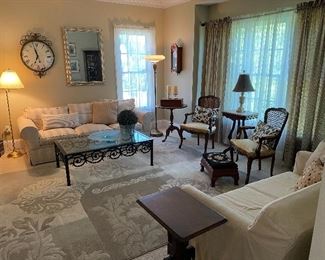 Living Room: wrought iron & glass coffee table, (sofa NFS), brass floor lamp, decorative wall clock, silver large wall mirror, (French side table, SOLD), Statue of Liberty Commemorative wall clock, pair antique French armchairs, slip covered loveseat, Victorian side table.