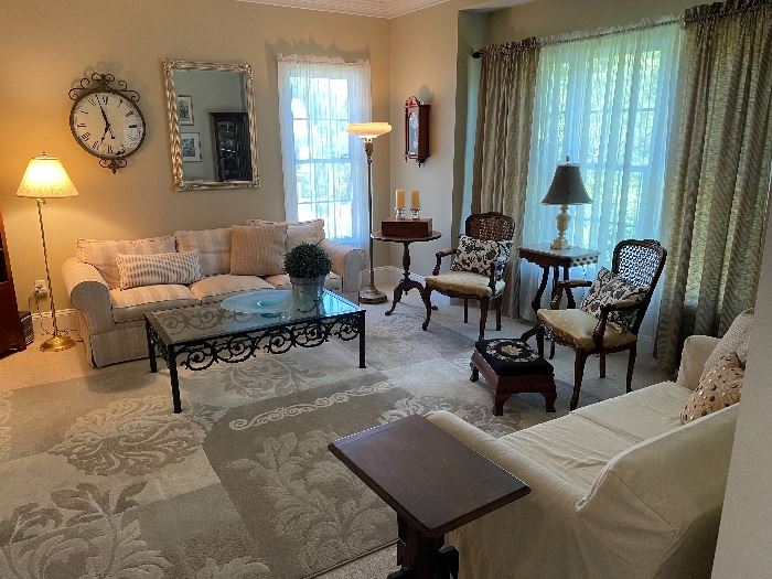 Living Room: wrought iron & glass coffee table, (sofa NFS), brass floor lamp, decorative wall clock, silver large wall mirror, (French side table, SOLD), Statue of Liberty Commemorative wall clock, pair antique French armchairs, slip covered loveseat, Victorian side table.