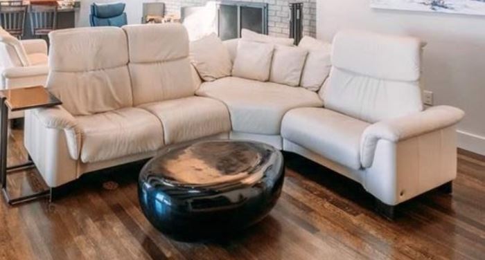 Ekornes Stressless sectional in ivory white leather. Three piece. 2-seat section 61" wide. One-seat section 36" wide. Middle section 54" wide. $2,800. River Stone Cocktail table with black gel coat. 40" long x 25" wide x 14" tall. $500