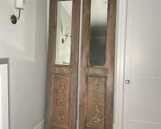 PAIR ANTIQUE CARVED DOOR MIRRORS | Originally sold by Pottery Barn; mango and mahogany wood with a hand-carved and hand-painted distressed finish made from an antique door, with beveled mirror glass; h. 98 x 22 in. 
