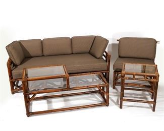 Lot 60 | (4PC) BIELECKY BROTHERS RATTAN SUITE | Comprising a sofa, a side chair with brass caps, a tiered side table (h. 23 x w. 40 x d. 18 in.), and a sofa end table (h. 24 x w. 20 x d. 16 in.); with cushions; h. 30 w. 32 d. 32 in. (chair); overall: h. 30 x w. 69 x d. 32 in. (sofa)