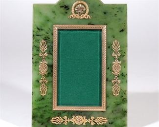 Lot 125 | RUSSIAN SPINACH JADE, DIAMOND & GOLD PICTURE FRAME | By Boris Roitman (20th century), designed as an easel back picture frame carved from a single piece of spinach jade with applied 14k yellow gold decor mounting melee diamonds, having a domed top crested by chased French wreath encircling boss, sides and bottom with anthemion, photo insert with chased feathery surround, the vermeil silver scrollwork easel back marked "925"; h. 4-3/4 w. 2-6/8 in. (insert); overall: 8-3/8 x 5-5/8 in. (frame) - Boris Roitman was trained in his native Russia by the last of Faberge's apprentices; although not an antique, it is truly unique