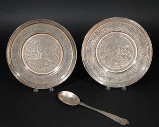Lot 264 | (3PC) IRANIAN SILVER PLATES & SPOON | Including a pair of 20th century Iranian silver plates with the "Armed Lion" hallmark, each highly decorated with a figural scene in the center within an Arabesque border (dia. 9-3/4 in.); plus a decorated serving spoon with the Farsi/Arabic "84" imitation of Russian mark (l. 10-1/4 in.); all together 32 ozt