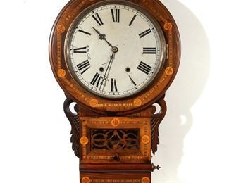 Lot 298 | WILLIAM IV NEO-GOTHIC INLAID SCHOOL WALL CLOCK | The case with inlaid cross devices and contrasting wood borders, with applied carvings flanking a lower hinged door of carved openwork wood behind glass, the face painted with Roman numerals
h. 28 w. 17 d. 4 in.