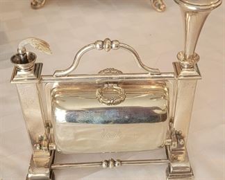 32.  $1400.00.  Really a rare find.  Staniforth patent table cigar lighter. Silver-plate cigar box/case to accommodate shorter cigars or cheroots.  Also doubles as an ashtray.  Circa 1900.  Fenton Bros.                                          
One end of the frame is the fuel chamber and the other end is a lighter wand which would have a piece of combustible material in the end and would be lit by the flame to light one's cigar.  Likely a commissioned item for a Regimental/ceremonial gentleman's  type dinner for its era.  England.