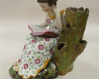 A STAFFORDSHIRE PEARLWARE SPILL VASE, IN THE FORM OF A SEATED WOMAN READING A BOOK. 7 1/8" TALL. Some spots of glaze missing on the green base, crack on the tip of the right toes. Back of stump repaired. ca 1815-1820