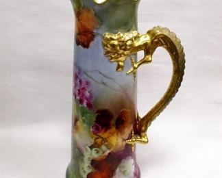 J.P.L. FRANCE (JEAN POUYAT LIMOGE) PORCELAIN TANKARD. HAND PAINTED OVERALL WITH GRAPE MOTIF, GOLD DRAGON FORM HANDLE. 14.5" TALL. Much gold paint has been applied to the handle, likely to cover areas of worn original