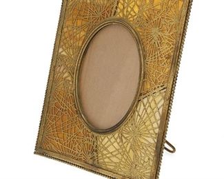 1020
A Tiffany Studios Gilt-Bronze Pine Needle Frame
Circa 1902-1919; New York, NY
Signed: Tiffany Studios / New York / 946
The rectangular gilt-bronze frame with white and amber mottled slag glass, pine needle motif gilt-bronze overlay, and beaded border enclosing an oval opening
Overall: 10" H x 8.125" W x 4.625" D; Opening: 5.25" H x 3.75" W
Estimate: $800 - $1,000