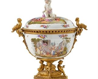 1057
A Continental Porcelain Urn
Late 19th/Early 20th Century
Appears unmarked
Possibly French with German porcelain, the round vessel with painted figural scenes and floral sprays, surmounted by a putto with wine, flanked by opposed putti handles, and raised on a bronze footed support with putti and laurel leaf border
19" H x 17" W x 12.5" D
Estimate: $3,000 - $5,000