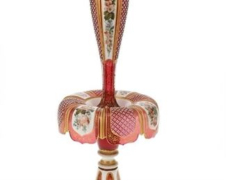 1064
A Bohemian Art Glass Epergne Centerpiece
Fourth-Quarter 19th Century
Underside rim with wheel engraved "XI"
The centerpiece with a detachable center vase set on a stand with turn-down collar, acid-cut from opaque white to translucent cranberry glass decorated with panels of polychrome floral sprays alternating with diamond-cut panels against a field of gilt highlights
15.5" H x 6.25" Dia.
Estimate: $1,000 - $1,500