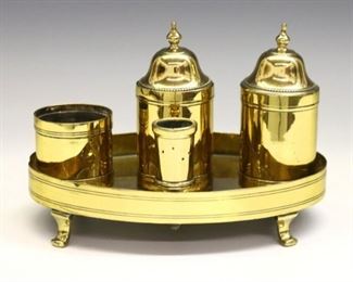 A 20th century Georgian style Brass standish.  Oval footed form with a central sander surrounded by two inkwells and candle holders.  Some surface wear and minor damage to Brass, misshaping at edges, missing one lid.  Approximately 7 x 5 x 5" high overall.  ESTIMATE $100-150
