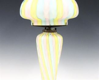 A 1970's Italian Rainbow Mother of Pearl art glass lamp.  Handblown mushroom form shade with baluster base in pastel Pink, Blue and Yellow "Diamond Quilted" pattern.  Electric cord marked "FMC Milano".  Slight surface wear, several scratches and hairline to base around re-glued Bronze mount, two production grooves at foot, wear at bottom rim of shade with two chips and edge roughness.  21 1/2" high.  ESTIMATE $200-400
