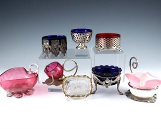 Eight Art Glass, Sterling and Silverplate salt cellars.  Various forms with frosted, Cranberry and Cobalt Blue glass.  Pierced cellar with Cranberry liner marked "Sterling".  Some wear overall, small chips to glass, gold filigree missing gems, smaller leaf form with repair to frame.  Up to 4" long and 3" high.  ESTIMATE $200-300
