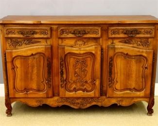 An early 20th century Country French Walnut buffet.  Parquet top with a shaped molded edge over three drawers with wrought iron handles and carved floral detail, over three doors with shaped panels and iron Cathedral hinges, scalloped apron with carved urn and short cabriole legs.  Older finish with some dents and minor damage.  70 x 24 x 43 1/2" high.  ESTIMATE $400-600