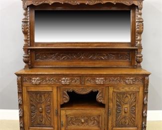 A late 19th century English carved Oak buffet.  Tall back with carved molded cornice over a beveled mirror with molded shelf and carved panel on a base with two carved silverware drawers over an open central shelf and lower door flanked by carved panel doors and corner pilasters on a base with carved molding. Older refinishing with some wear, losses to base molding.  72 x 22 x 79 1/2" high.  ESTIMATE $800-1,200
