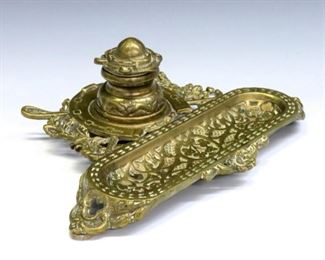 A 19th century Aesthetic Period Brass inkstand with equestrian design.  Single inkwell with porcelain liner and pen tray, features a jockey cap form lid and horseshoe stand with elaborate whip and floral design.  Impressed "2214".  Some surface wear, oxidation and slight pitting.  10 x 8 x 3 1/2" high overall.  ESTIMATE $200-300