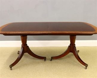 A Baker Hepplewhite style dining table.  Mahogany construction with Kingwood and Satinwood banding.  Rounded top with three leaves having reeded edges on a two pedestal base with turned columns and three saber legs with reeded detail and Brass castors.  Very slight wear.  Includes custom table pads.   46 x 76 (plus 3 x 19" leaves = 135" total) x 29 1/2" high overall.  ESTIMATE $1,000-2,000