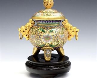 A Chinese Cloisonne censer.  Round form with multicolor floral decoration, Gilded detail and dragon form handles on tapered tri-pod legs.  Minor wear.  6" high plus wooden stand.  ESTIMATE $200-400