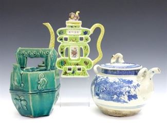 Three Asian porcelain and earthenware teapots.  Includes a Famille Verte "puzzle" teapot in Shou Character form with polychrome decoration and Foo Dog lid, a Shiwan Ware teapot in hexagonal form with Green glaze and animal/insect decoration in relief, and a Blue and White transferware teapot in round form with hand-painted lid.  Some wear overall, Shou Character with repaired rim and small chip to spout, Shiwan Ware with crazing and surface wear, Blue and White with hairlines to bottom and lid, chips to spout and lid liner.  7 3/4" to 9" high.  ESTIMATE $400-600