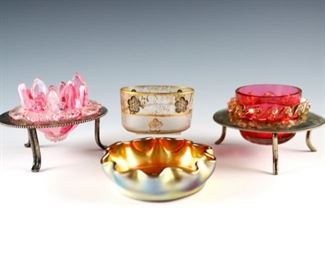 Four early 20th century Art Glass salt cellars.  Includes a Tiffany Favrile glass salt with Golden iridescent finish and ruffled rim, a Daum cameo glass salt with Gilded floral decoration, and two Cranberry Art Glass salts with Silverplate holders.  Incised "LCF Favrile" and "Daum Nancy" with Cross of Lorraine.  Some wear to surface and Gilding, chip to bottom of Daum and lotus flower, tiny flake to other Cranberry glass rim.  Up to 3" long and 2 1/2" high.  ESTIMATE $400-600