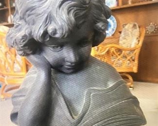 Short statue of child reading a book.