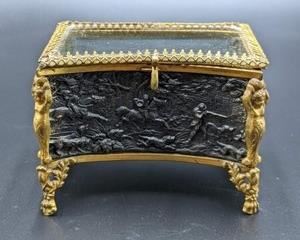 Vintage Glass and Bronze Jewelry Box featuring a lovely embossed scene with figurines on the corners. The top lid sits crooked and there is some wear to the inner lining. Measures 5” x 3” and 3.5” high.
