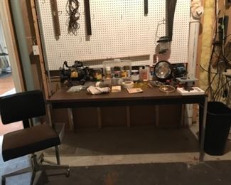 Lower Level-Tool Room:  An assortment of paints/stains/varnishes are near a  portable spot light; a  4-inch table saw; OHIO FORGE 6" inch bench grinder; LITTLE GIANT 5-MSP 1/6 HP submersible only pump; and other tools are displayed on a chrome/wood top desk.  To the left is an office chair on casters, while a saw, level, and other items hang on the peg board.