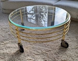 Round Glass Topped Coffee Table. Cool rolling coffee table! There is some light wear on the brass paint and the top glass has some scratches. Measures 38” in diameter and 18” high. 