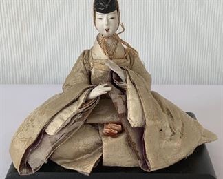 Lovely antique Asian doll figurine sitting on a stand. Her dress has some condition issues including some rips/tears.