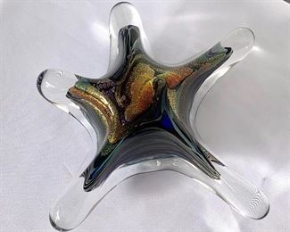 Beautiful Star Shaped Art Glass by Rollin Karg. The star rests on a metal stand giving it a magical floating look. Signed by the artist on the back and dated 2003. The back where the hole is to fit into the stand has a small chip which is to be expected from the star being placed on the stand.  Measures a bout 9” h x 8” w 