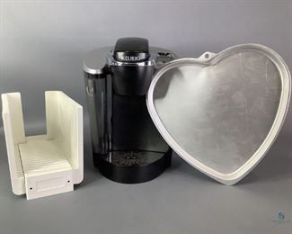 Keurig & More
Includes a Keurig single cup coffee maker model E60, a West Bend bread loaf slicer, and a Wilton heart shaped cookie pan. Scuffs on Keurig.