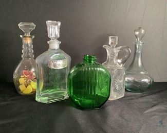 Decorative Glass Decanters
Five total decanters, one without stopper. One dark green cut glass decanter. One curved bottom light blue glass decanter. One square cut glass decanter with pour spout and square shaped stopper. One clear glass oblong shaped bottom with narrow stopper. One square shaped clear glass decanter with pewter Gin label and stopper. Tallest is 10.5"H.