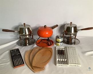 Fondue Sets
Three fondue pots. Two are matching silver tone metal with wood handles. Comes with tray, stand and covered heat source container. One orange ceramic/porcelain over metal pot with matching tray and dark metal stand. It has chips in the finish and wood handle shows wear. Also includes 3 sets of wooden serving plates and fondue forks.