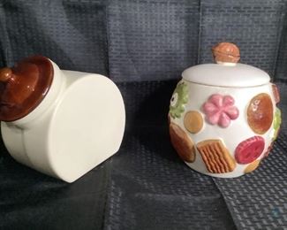 Vintage Cookie Jars
One 1950's -1960's Napco ceramic cookie jar with walnut shaped handled lid. Jar has a multi-colored cookie design on the outside. One cream colored ceramic cookie jar with brown lid. Jar shows crazing.