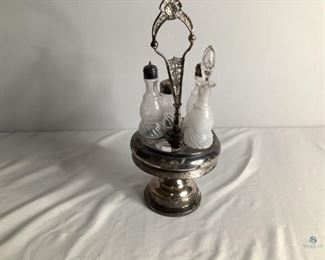 Victorian Cruet Condiment Set.
Silver colored metal pedestal stand with attached handle. Comes with five glass containers that have an etched design, three have metal and one is a glass stopper. Two of the glass containers have chipped rims. Metal handle is bent. Metal stand shows wear. 17"Hx7"W