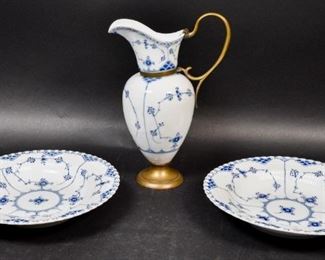 86	3 Pieces of Royal Copenhagen Blue Fluted Porcelain	3 pieces of Royal Copenhagen blue fluted porcelain. 2 full lace bowls and a ewer with later brass fittings. Bowls with a contemporary mark on the underside. Ewer with 18th-19th century 3 wave under glaze mark with the number "96"on the right side. Ewer: 10 3/4"H. Bowl: 10" Diameter.
