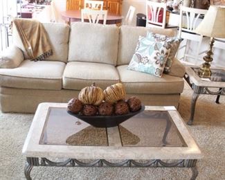 Living room area has glass top iron base coffee table, two end tables and a clean, neutral sofa.  