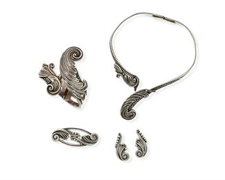 318
A Group Of Margot De Taxco Silver Jewelry
1948-1978; Taxco, Mexico
Each stamped: Margot de Taxco / Sterling / Made in Mexico / [Eagle 16]; Each further stamped with design number
Designed by Margot Van Voorhies, comprising a crossover hinged bangle in a stylized foliate design No. 5339 (6.5" inner C x 3" H), a foliate design hinged collar necklace No. 5338 (13" inner C x 2.25" H), and a foliate-style brooch No. 5337 (1" H x 2.375" W) with a matching pair of ear clips (1.5" L)

5 pieces
180.0 grams gross
Estimate: $500 - $700