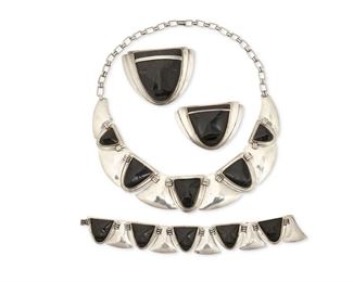 338
A Group Of Abraham Paz Silver Jewelry
Circa 1940-1950; Mexico City, Mexico
Each stamped: AP / Sterling / Mexico
Comprising a necklace with obsidian and triangular silver links (16" L x 1.25" H), an onyx and silver mask bracelet of similar design (6.25" L x 0.875" H), a half-round onyx set mask brooch (2" H x 2.5" W), and a smaller onyx set mask brooch (1.5" H x 2.25" H)

4 pieces
170.4 grams gross
Estimate: $500 - $700