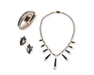 345
A Group Of Sigi Silver, Enamel, And Stone Jewelry
1952 or later; Taxco, Mexico
Each stamped: SIGI / Tasco / Hecho en Mexico / Sterling / [Eagle 3]; Each further variously stamped with design number
Designed by Sigfredo Pineda, comprising of a necklace of double-sided inlaid stone graduated drops on a strand of silver balls No. 299 (15.5" L x 1.625" H) and a hinged cuff bracelet with enamel accent and tiger's eye stone No. 84 (6.75" inner C x 1.375" H) with matching enamel and tiger's eye ear clips (1.25" L)

3 pieces
126.6 grams gross
Estimate: $300 - $500