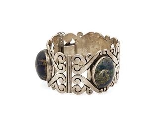 357
A Mexican Silver And Green Stone Link Cuff Bracelet
Mid-20th Century; Taxco, Mexico
Stamped: ARS / Cuauthemoc / Taxco / Silver
A wide link chased silver bracelet set with three large oval cabochon blue and green stones with heavy matrix, with clasp closure and chain guard
7" inner C x 1.625" H
124.7 grams
Estimate: $100 - $200