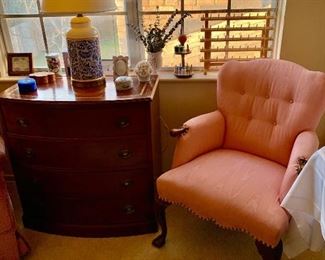 A fantastic  tufted pink armchairwith claw and ball feet next to leather topped mahogany bow front chest 